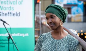 Warda Yassin, a young Somali-British woman, smiles to the side. She wears a green headscarf and a green dress.